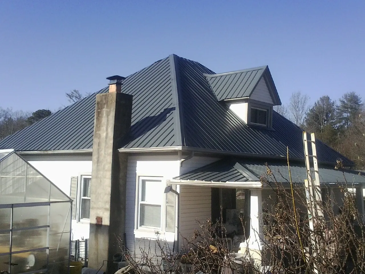 Dark blue standing seam metal roof on a white farmhouse with dormer — Slate & Tile Roof Repair by Roofing Brothers in Coburn