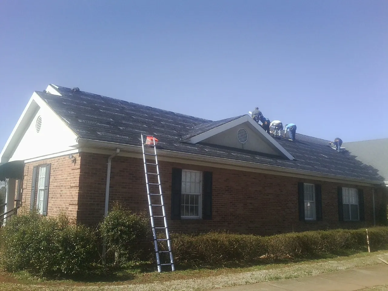 Crew tearing shingles off a brick ranch roof with a ladder set — Emergency Roof Repair work by our crew in Coburn