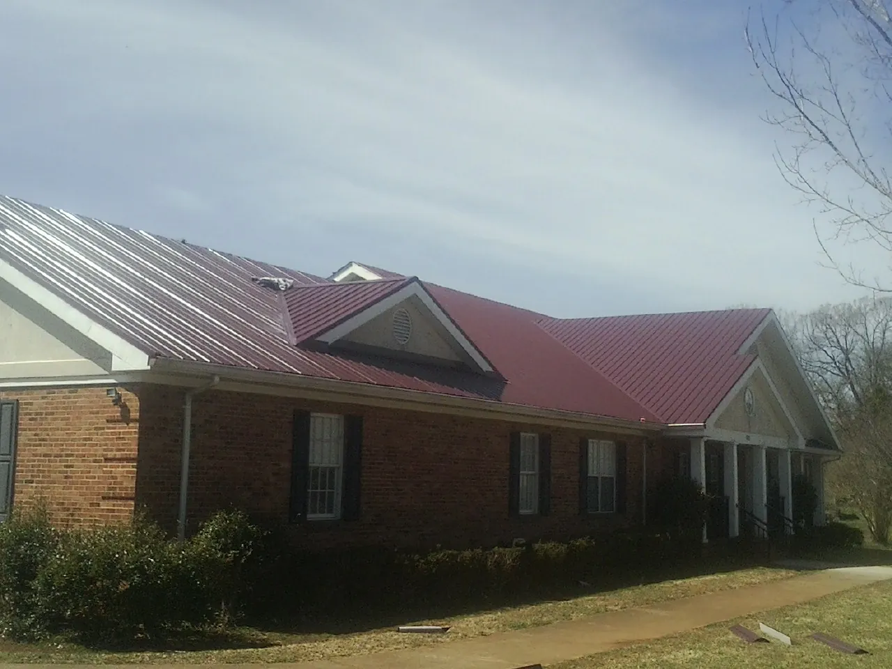 Red metal roof with gabled entries on a long brick building, from a Hail Damage Roof Repair job in Coburn