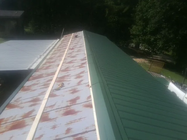 Old rusted panels beside newly installed green metal roofing — Wind Damage Roof Repair by Roofing Brothers in Coburn
