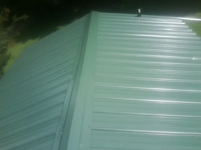 New green metal panels meeting at the ridge of a roof — Flat Roof Repair work by our crew in Coburn