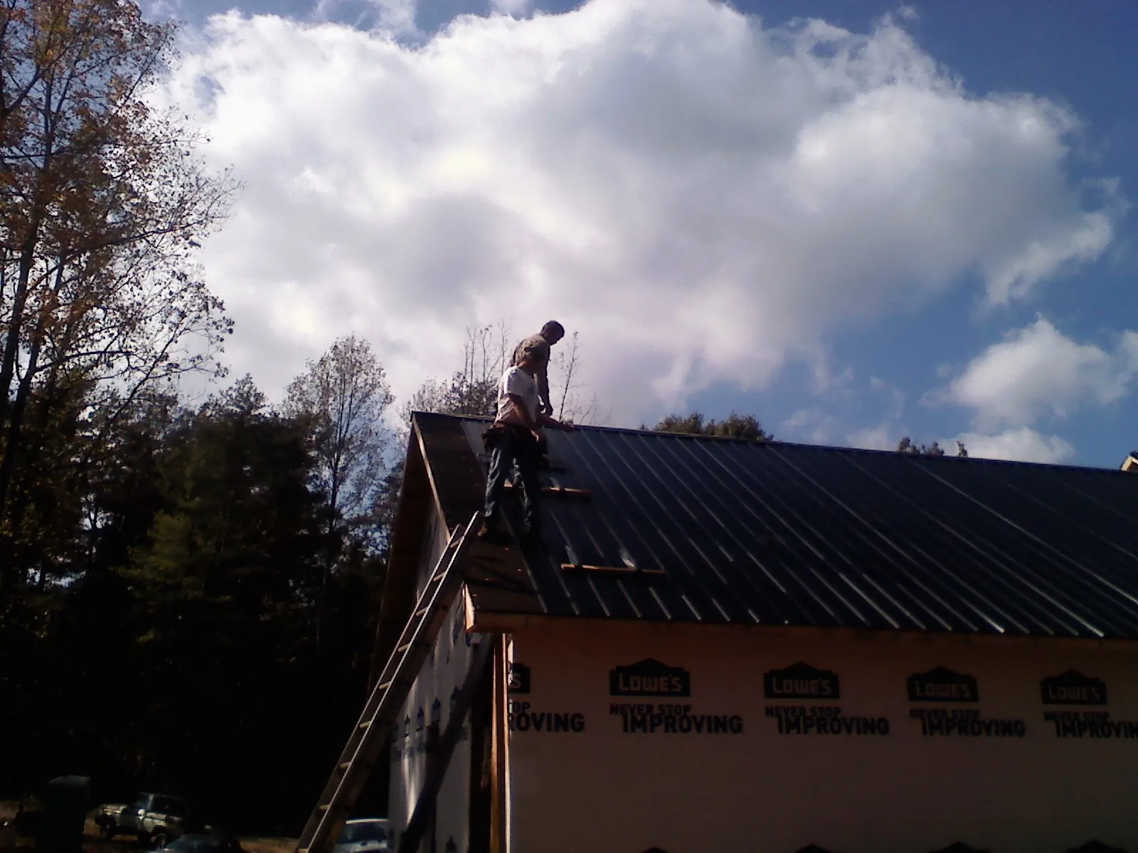 Roofer fastening dark metal panels high against a cloudy sky, from a Roof Inspection job in Coburn