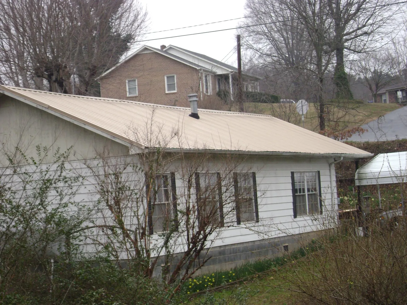 Tan metal roof on a white sided house set into a hillside — Commercial Roofing by Roofing Brothers in Coburn