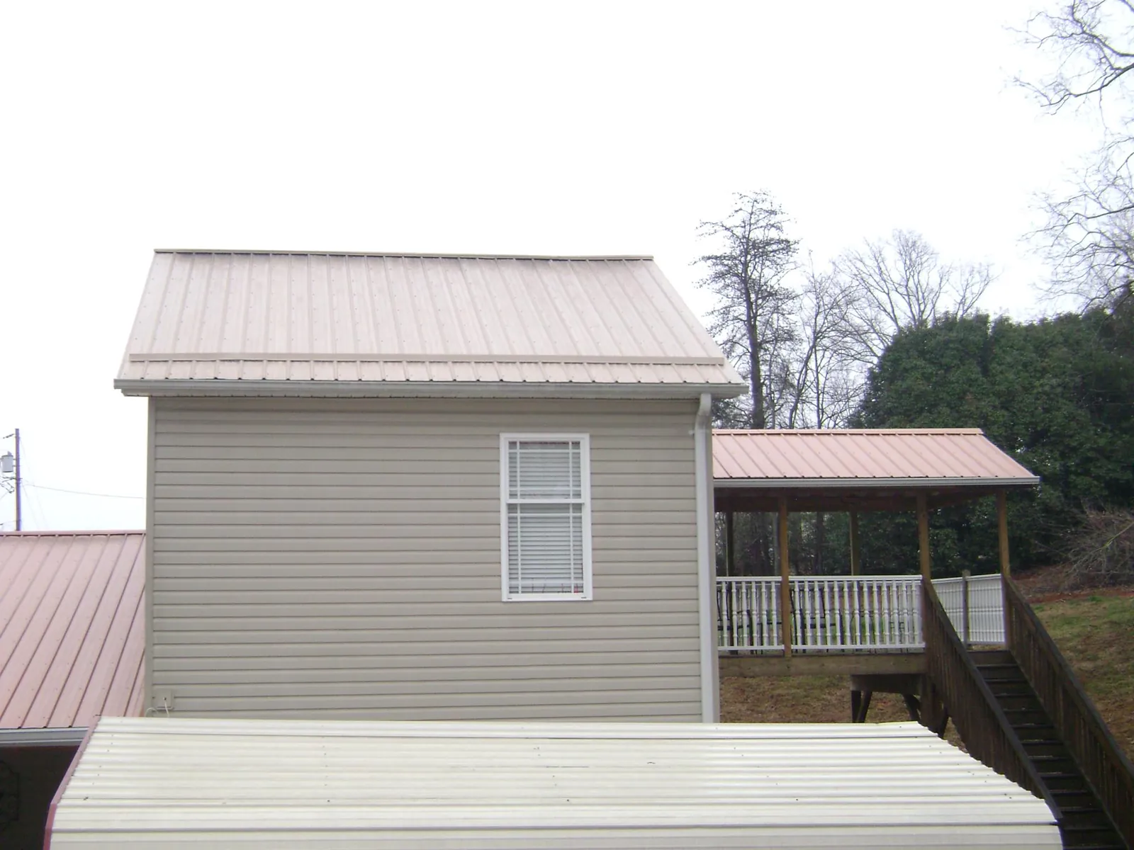 Tan metal roofs on a two story addition and attached porch, from a Roof Replacement job in Coburn