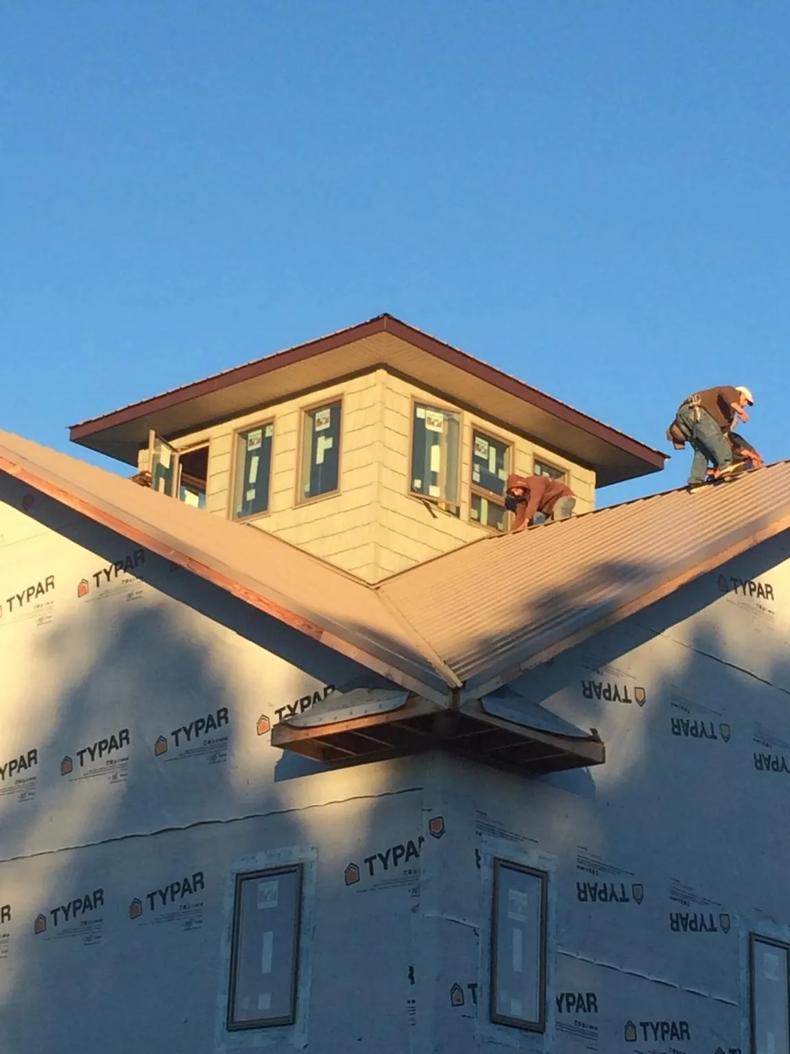 Roofers working around a rooftop cupola on a new metal roof at sunset — Roof Waterproofing in Coburn by Roofing Brothers